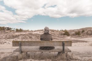 Older person sitting on bench near sand dunes